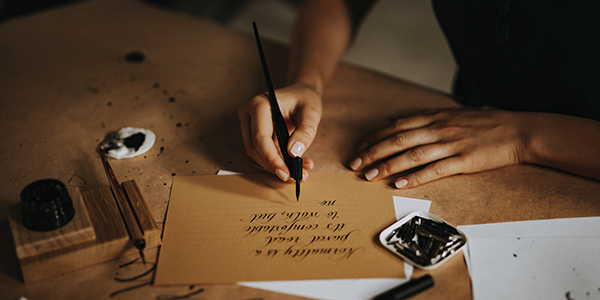 Person writing on a card at a desk with low lighting.